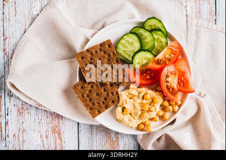 Gros plan de platte avec houmous, pois chiches, tomate, concombre et craquelins de grain sur une plaque vue de dessus Banque D'Images