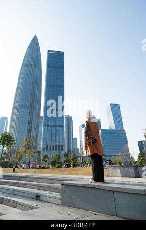 Femme âgée debout sur les marches surplombant les gratte-ciels modernes dans le paysage urbain sous un ciel bleu clair Banque D'Images