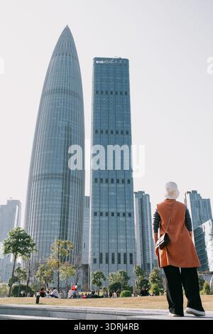 Femme en manteau orange debout devant les gratte-ciel modernes dans le paysage urbain sous ciel clair Banque D'Images
