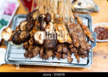 Brochettes grillées avec champignons et viande sur plateau métallique, cuisine de rue asiatique, vue rapprochée sur la table en bois Banque D'Images