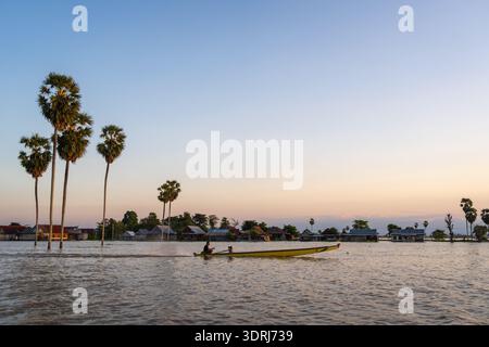 Un pêcheur traditionnel de Bugis navigue son bateau sur le lac Tempe au coucher du soleil, entouré de palmiers et d'une maison flottante de village Banque D'Images