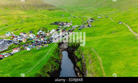 Vue aérienne à couper le souffle d'un village pittoresque niché dans les collines verdoyantes des îles Féroé Banque D'Images