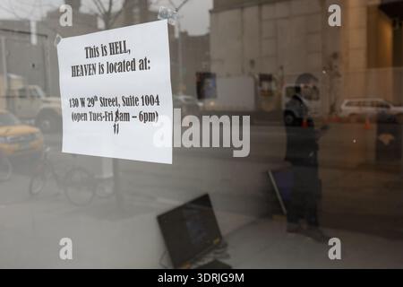 Un panneau humoristique dans une fenêtre de la 9ème Avenue dit "C'est L'ENFER, LE PARADIS est situé au : 130 W 29th Street," New York City. Banque D'Images