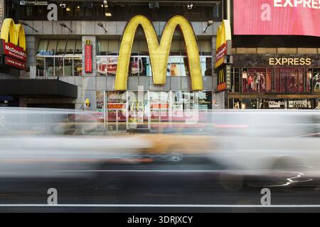 Les arches dorées emblématiques d’un restaurant McDonald’s à Times Square, Manhattan, avec le flou de mouvement du trafic urbain. Banque D'Images