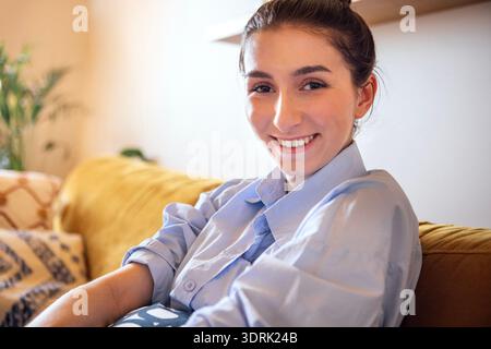 Portrait en gros plan d'une fille mignonne dans une chemise bleue sur le canapé dans le salon. Un adolescent est souriant et assis sur le canapé Banque D'Images