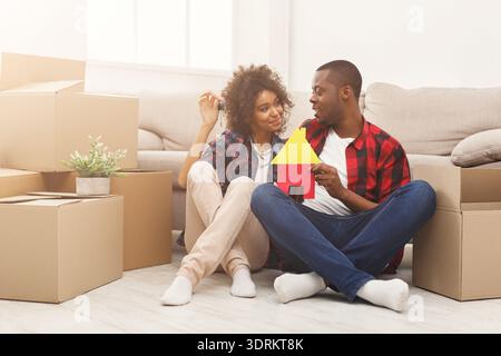 Couple est assis sur le sol parmi les boîtes tout en tenant un modèle d'une maison dans New Home Setup Banque D'Images