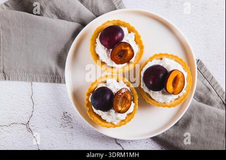 Gros plan de mini tartelettes avec fromage cottage et prune sur une assiette sur la vue de dessus de table Banque D'Images