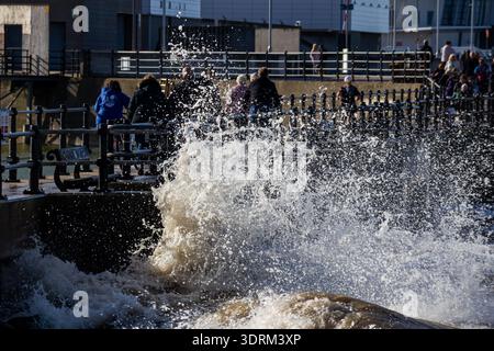 Les gens marchent le long de la promenade à New Brighton alors que la grande vague d'onde de tempête s'écrase au-dessus de la digue Banque D'Images