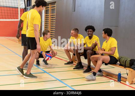 Divers coéquipiers masculins de volley-ball dans des chemises jaunes shorts noirs se reposant, bavardant sur le court près du filet. Athlètes, travail d'équipe, sport, Banque D'Images