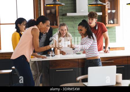 Dans la cuisine, les adolescents fêtent avec enthousiasme et regardent le papier, partageant un moment joyeux. Fête, bonheur, adolescents, excitème Banque D'Images