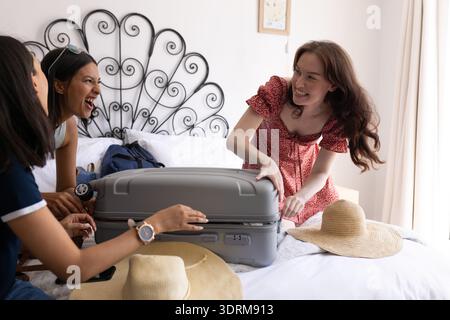Emballant la valise sur le lit, trois jeunes femmes rient ensemble. Ils se préparent pour un voyage amusant, partageant l'excitation et Wearin Banque D'Images