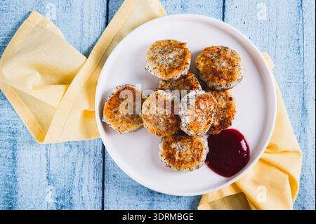 Gros plan de mini crêpes au fromage cottage avec des graines de pavot et de la confiture de baies sur une plaque vue de dessus Banque D'Images