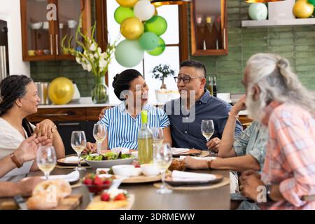 À la maison, des amis seniors ayant du vin et discutant pendant la réunion de fête. Socialisation, amitié, célébration, hospitalité, leis Banque D'Images