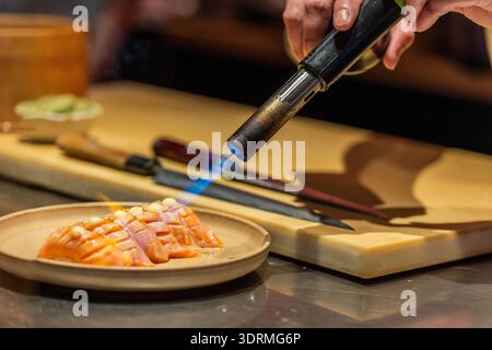 Chef utilisant la torche pour caraméliser le filet de saumon sur une planche à découper en bois Banque D'Images