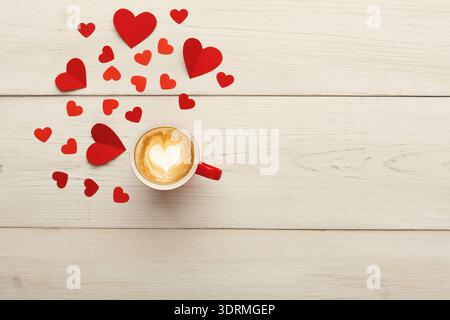 Tasse à café avec coeur Latte Art entouré de coeurs en papier rouge sur la table en bois Banque D'Images