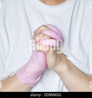 Gros plan de la personne en chemise blanche avec les mains attachées portant des gants roses Banque D'Images