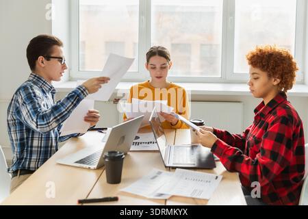 Brainstorming sur le travail d'équipe. Divers collègues qui travaillent ensemble discutent des statistiques financières. Groupe de jeunes heureux gens modernes sittin Banque D'Images