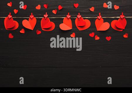 Les coeurs rouges forment un collage sur une corde avec de petits coeurs dispersés sur un fond sombre Banque D'Images