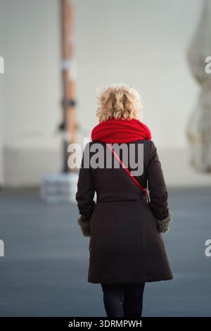 femme senior blonde avec écharpe rouge marchant dans la rue à alghero vue de derrière Banque D'Images