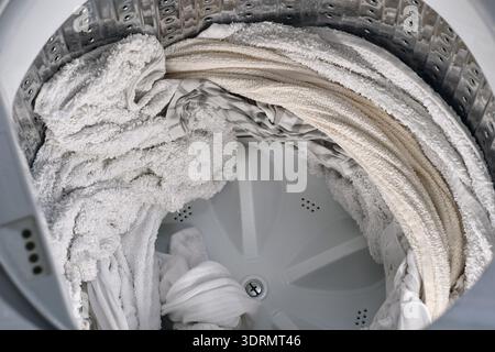 Voir l'intérieur du tambour de lave-linge à chargement par le haut rempli de linge blanc humide essoré après le cycle de lavage. Concept de corvée domestique, textiles propres, entretien des tissus, Banque D'Images