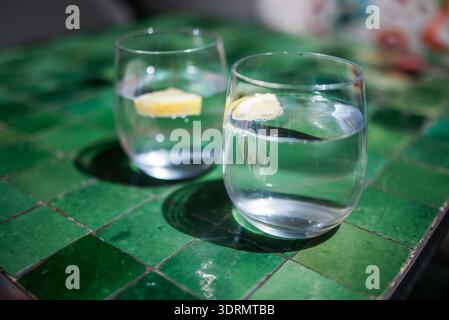Deux verres d'eau clairs avec des tranches de citron assis sur une table carrelée verte vibrante, mettant en vedette des boissons rafraîchissantes dans un et lumineux Banque D'Images