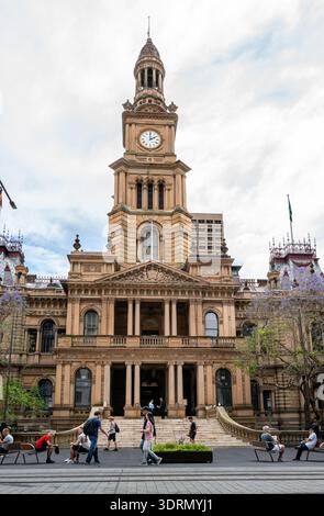 La façade historique en grès et la tour de l'horloge de l'hôtel de ville de Sydney sur George Street pendant la saison printanière de Jacaranda. Banque D'Images