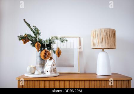 Arrangement décoratif avec une lampe élégante, un vase festif avec de la verdure et une charmante maison miniature sur une table en bois, Banque D'Images