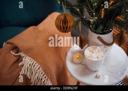 Scène hivernale confortable avec une couverture chaude, une tasse de guimauves, des ornements décoratifs et une bougie, créant une atmosphère festive Banque D'Images