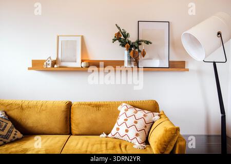 Salon confortable avec un canapé jaune moutarde orné d'oreillers décoratifs, une étagère en bois affichant un décor minimaliste, un Banque D'Images