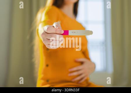 Main de femme tenant un test de grossesse positif. Femme enceinte avec gros ventre attendant bébé subissent un traitement d'infertilité Banque D'Images