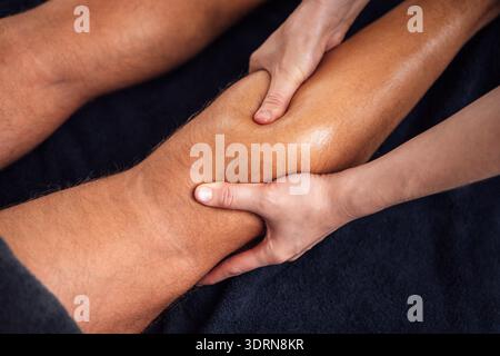 Massothérapeute qualifié appliquant une pression sur la jambe d'un client pendant une séance thérapeutique, présentant des techniques de relaxation et Banque D'Images