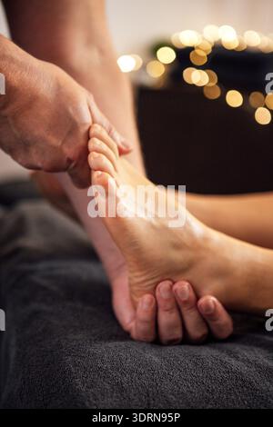 Gros plan d'une main qualifiée effectuant un massage relaxant des pieds sur un client, mettant en valeur l'atmosphère apaisante avec un éclairage doux Banque D'Images