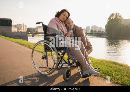 Femme âgée en fauteuil roulant marchant avec le soignant vieil homme sur la route. Homme de couple de vieillards soutenant la prise en charge des paralysés Banque D'Images