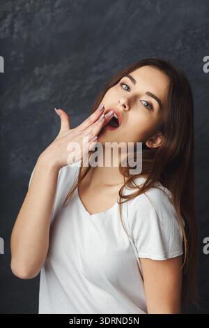 Femme posant avec la main sur la bouche dans un cadre décontracté sur fond sombre Banque D'Images