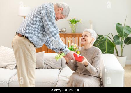 Homme senior donnant des fleurs boîte cadeau à la vieille femme. Heureux couple familial. Mari épouse avec cadeau tulipe fleurs bouquet célébratin Banque D'Images