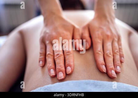 Mains d'un thérapeute de massage qualifié appliquant la pression sur le dos d'un client, mettant en valeur les techniques de relaxation et le guichet automatique apaisant Banque D'Images