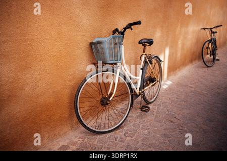 Vélo vintage avec un panier bleu appuyé contre un mur texturé, mettant en valeur le charme urbain et une atmosphère nostalgique dans un sunli Banque D'Images