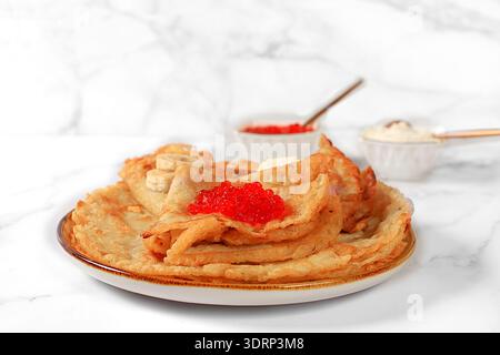 Délicieuses crêpes russes avec du fromage à pâte molle, des bananes et du caviar rouge sur la table de la cuisine. Un petit déjeuner sain fait avec i frais Banque D'Images