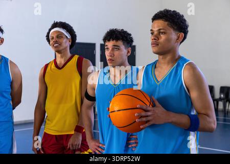 Divers coéquipiers masculins posant sur le terrain de gym tenant des maillots de basket-ball orange, espace copie. Athlètes, travail d'équipe, dynamique, a Banque D'Images