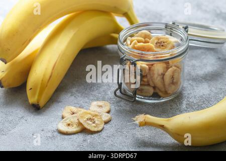 Chips de bananes séchées maison dans un bocal en verre et bananes fraîches. Tranches de fruits jaunes frits. En-cas sucré sain. Végétarisme Banque D'Images
