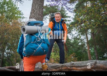 Aventure de randonnée. Homme aidant la main femme sur la randonnée dans la forêt. Couple senior appréciant la randonnée de loisirs en plein air. Vieilles personnes heureuses Banque D'Images