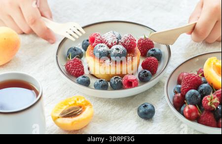 Crêpes au fromage cottage, syrniki, beignets de caillé avec des baies fraîches (framboise, myrtille, abricot) et sucre en poudre dans un blanc Banque D'Images