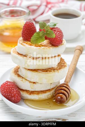 Crêpes au fromage maison avec miel et framboises fraîches. Petit déjeuner traditionnel savoureux et sain. Mise au point sélective Banque D'Images