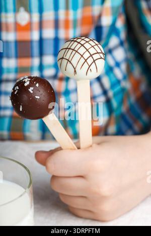 Deux cake pops décoré de chocolat blanc et noir dans les mains des enfants. Dessert pour les petits gourmets. Selective focus Banque D'Images