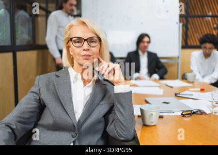 Portrait d'une femme d'affaires chef d'équipe féminine au bureau, des collègues se réunissant en arrière-plan. Chef d'entreprise souriant et confiant Woma Banque D'Images
