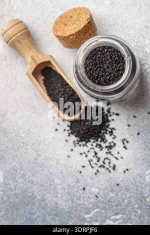 Graines de cumin noir sur une cuillère en bois et dans un bocal en verre sur fond gris Banque D'Images