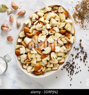 Champignons porcini frais crus tranchés dans une assiette blanche sur un fond de marbre. Les ingrédients de la marinade sont le sel, le poivre noir, Banque D'Images