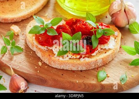 Bruschetta avec tomates cerises cuites au four, fromage à la crème (fromage cottage ou ricotta), ail, basilic frais et épices gros plan. Medite Banque D'Images
