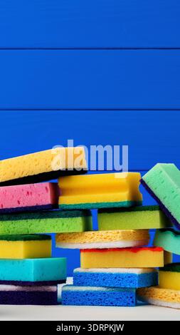 Éponges colorées empilées sur une table devant un fond bleu dans un arrangement simple Banque D'Images