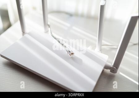 Prise de vue en grand angle d'un routeur Internet sans fil et d'un câble réseau sur une table en bois blanc. La scène dispose d'un design minimaliste et lumineux Lig naturel Banque D'Images